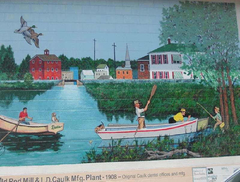 Mural depicting skiffs on the water in fornt of a downtown scene