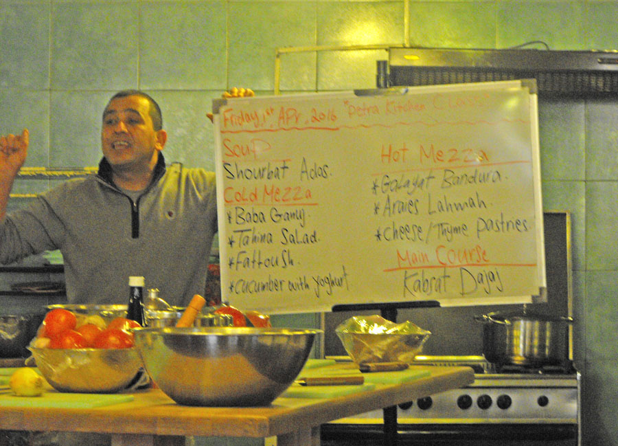 Petro Kitchen's manager, Ali, holding menue sign and bowls of food on table
