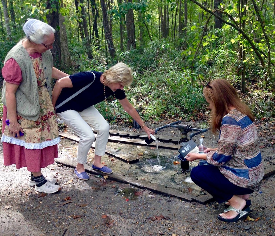 Three women getting a cup of water from God’s Acre Healing Springs 