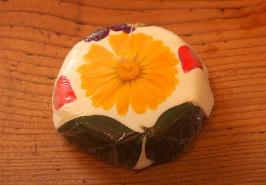 Cheese decorated with yellow edible flower, red petals and green herb leaves