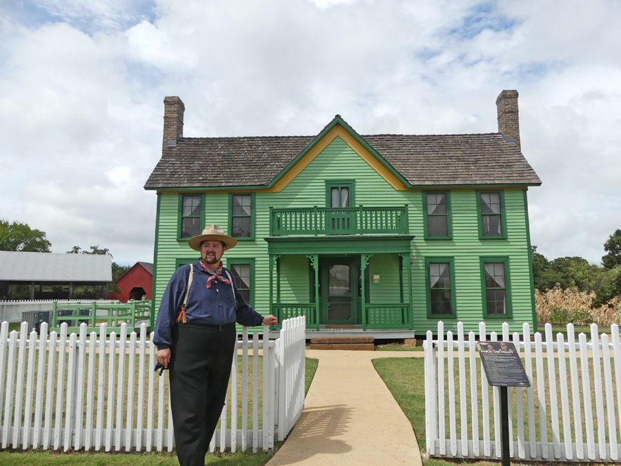 Docent stands at gate in front of farmhouse and welcomes visitors at Nash Farms