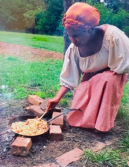 costumed female docent cooking over a open fire
