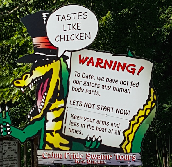 Cajun Pride Swamp tour sign with alligator holding message To date we have not fed our gators any human body parts. Lets not start now.