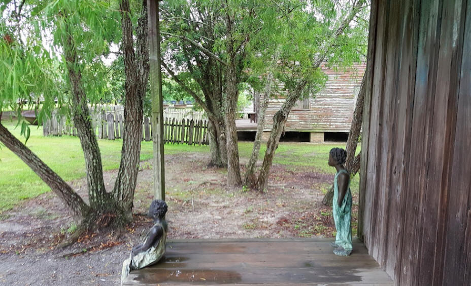 sculpture of two slave children on porch of cabin